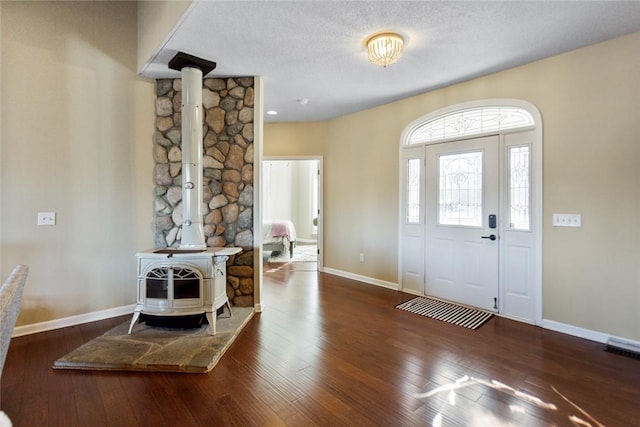 entryway with a wood stove, dark wood-type flooring, and a textured ceiling