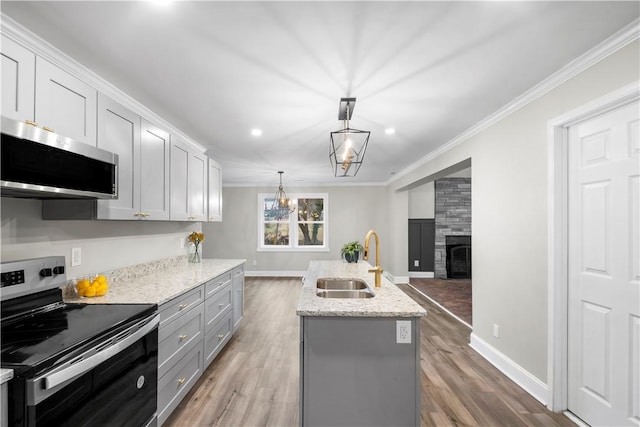 kitchen with a center island with sink, sink, hanging light fixtures, ornamental molding, and stainless steel appliances