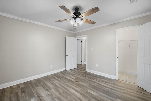 unfurnished bedroom featuring ceiling fan, a spacious closet, light hardwood / wood-style flooring, crown molding, and a closet