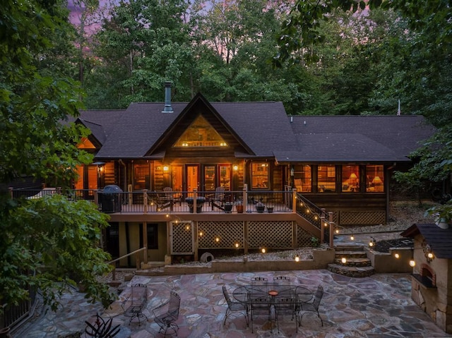 back house at dusk featuring a patio, a deck, and an outdoor fireplace