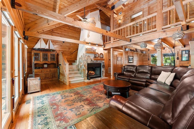 living room featuring high vaulted ceiling, wooden walls, light hardwood / wood-style flooring, ceiling fan, and beamed ceiling