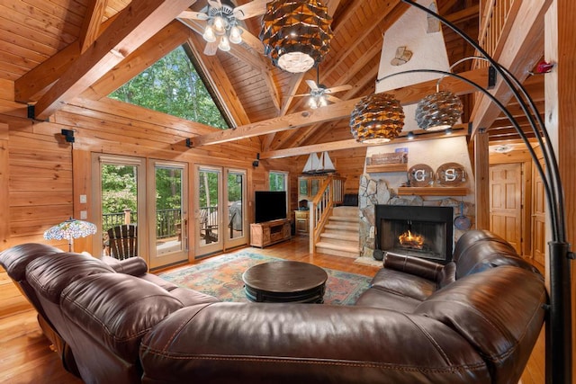 living room with wood walls, light hardwood / wood-style flooring, ceiling fan, a fireplace, and beamed ceiling