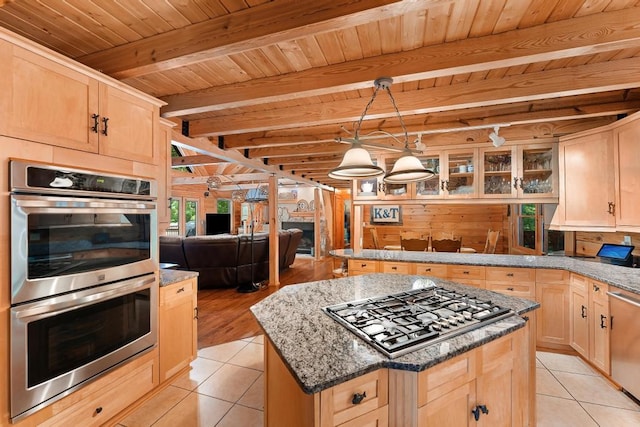 kitchen with light brown cabinets, dark stone countertops, beam ceiling, appliances with stainless steel finishes, and a kitchen island