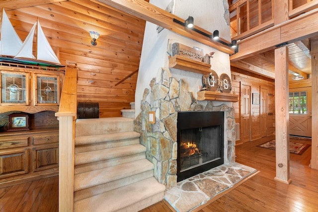 stairs with a stone fireplace, wooden walls, and wood-type flooring