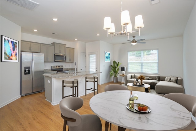 dining space featuring ceiling fan with notable chandelier, sink, and light hardwood / wood-style flooring