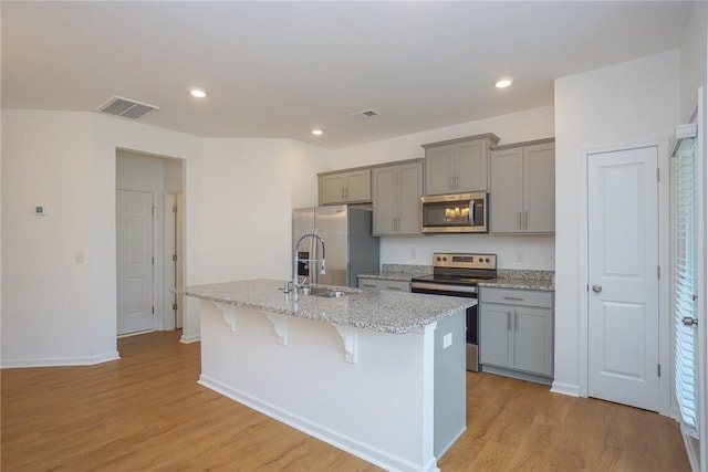 kitchen featuring gray cabinetry, stainless steel appliances, a kitchen breakfast bar, a kitchen island with sink, and light wood-type flooring