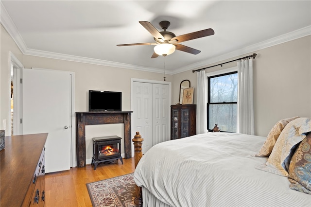 bedroom with a wood stove, ceiling fan, light hardwood / wood-style flooring, a closet, and ornamental molding