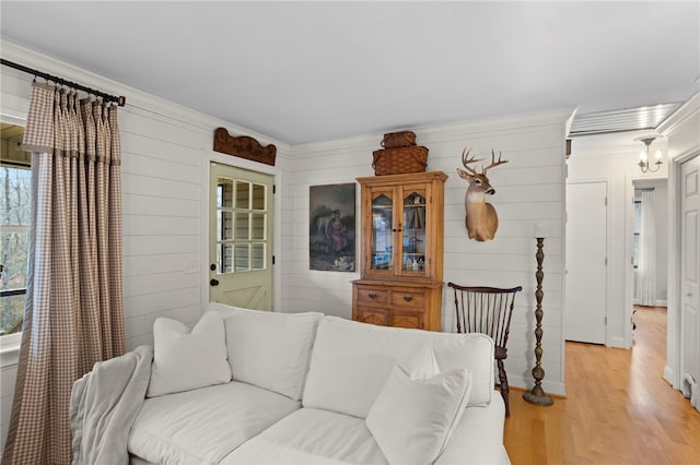 living room featuring light wood-type flooring, ornamental molding, and wood walls