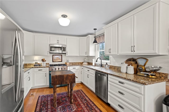 kitchen featuring sink, dark stone countertops, pendant lighting, white cabinets, and appliances with stainless steel finishes