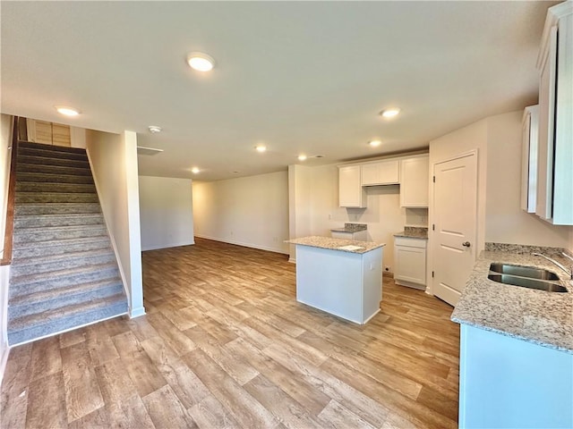 kitchen with light stone counters, sink, a center island, and white cabinets