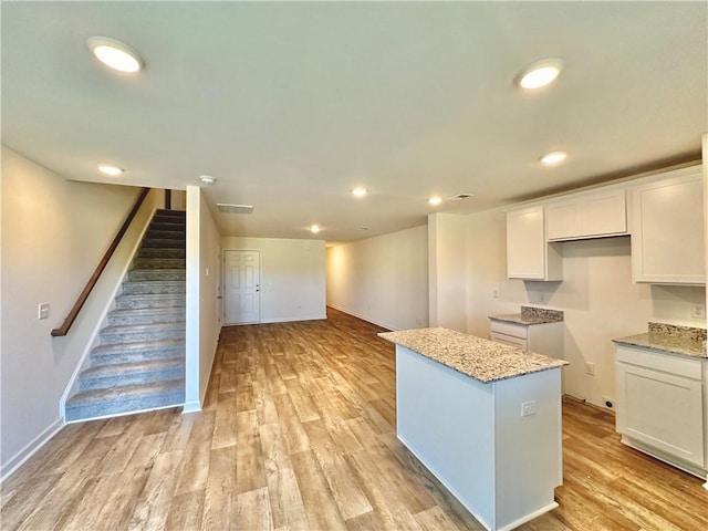 kitchen featuring white cabinetry, a center island, light stone counters, and light wood-type flooring