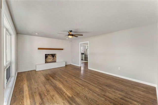 unfurnished living room with a wealth of natural light, ceiling fan, dark wood-type flooring, and a brick fireplace