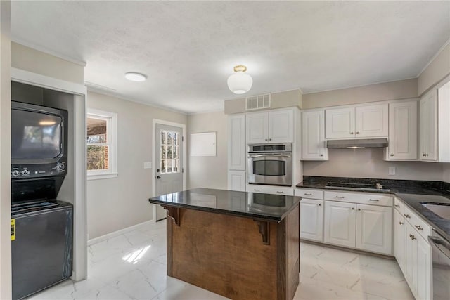 kitchen featuring stacked washing maching and dryer, stainless steel appliances, sink, white cabinets, and a kitchen island