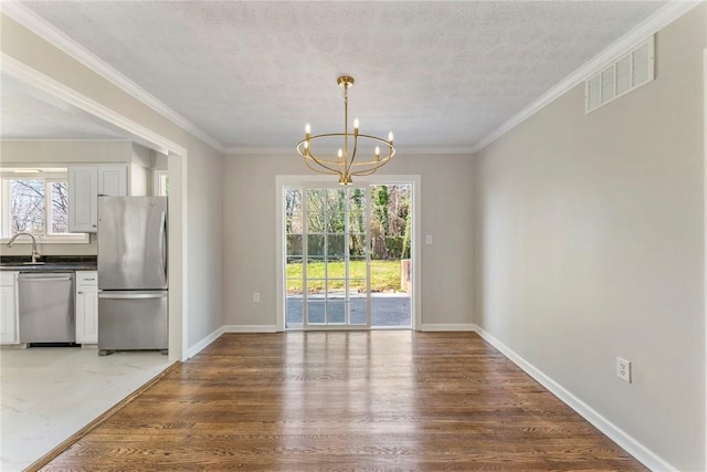 unfurnished dining area featuring sink, crown molding, a textured ceiling, wood-type flooring, and a chandelier