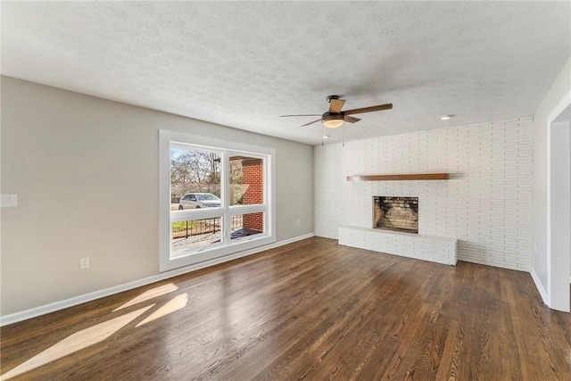 unfurnished living room featuring a textured ceiling, a brick fireplace, ceiling fan, and dark wood-type flooring