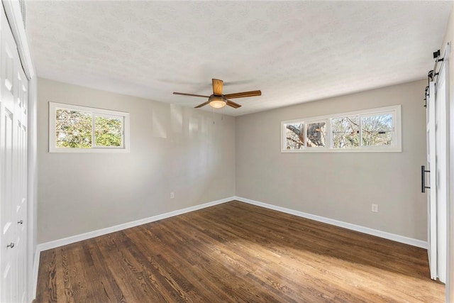 empty room featuring a barn door, ceiling fan, a textured ceiling, and hardwood / wood-style flooring