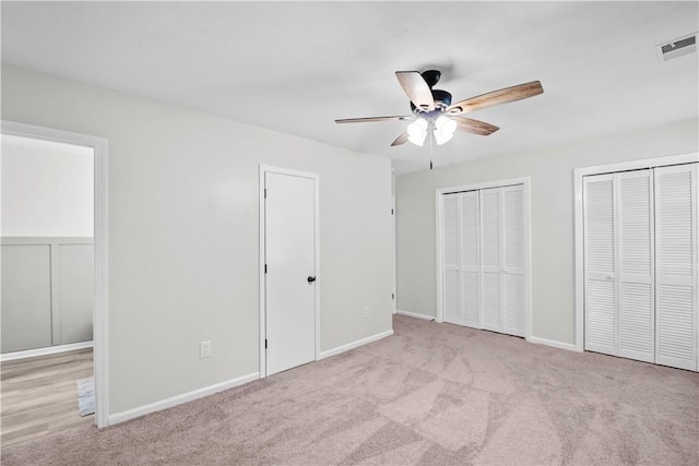 unfurnished bedroom with ceiling fan, light colored carpet, and two closets