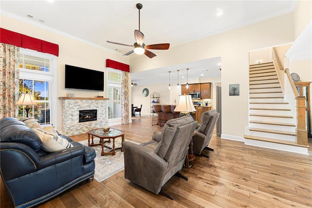 living room featuring ceiling fan, a stone fireplace, plenty of natural light, and light hardwood / wood-style flooring