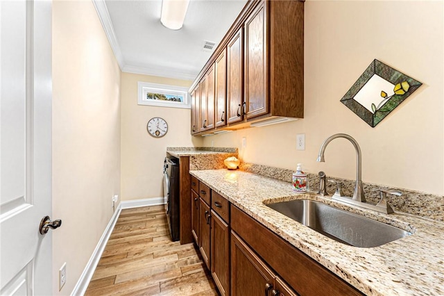 kitchen featuring sink, light stone counters, ornamental molding, washer and dryer, and light wood-type flooring