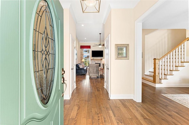 foyer entrance featuring a stone fireplace, crown molding, wood-type flooring, and ceiling fan with notable chandelier