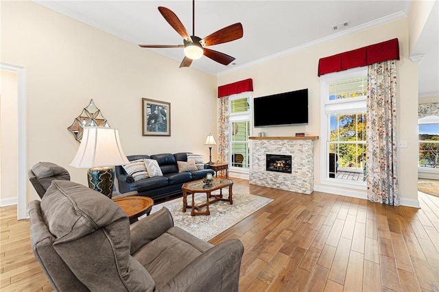 living room featuring a stone fireplace, ceiling fan, crown molding, and wood-type flooring