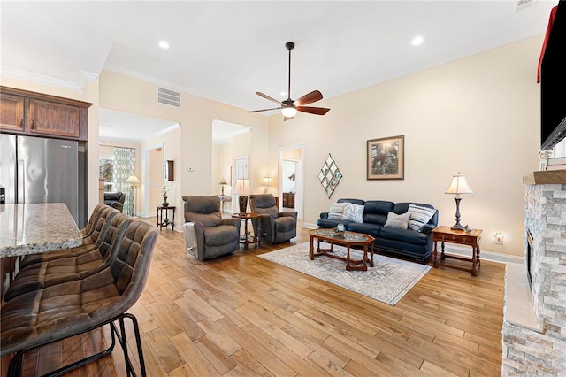 living room with a brick fireplace, ceiling fan, crown molding, and light hardwood / wood-style flooring