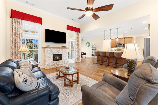 living room featuring ceiling fan, ornamental molding, a fireplace, and light hardwood / wood-style flooring