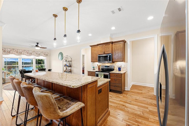 kitchen featuring pendant lighting, crown molding, ceiling fan, a kitchen island, and stainless steel appliances