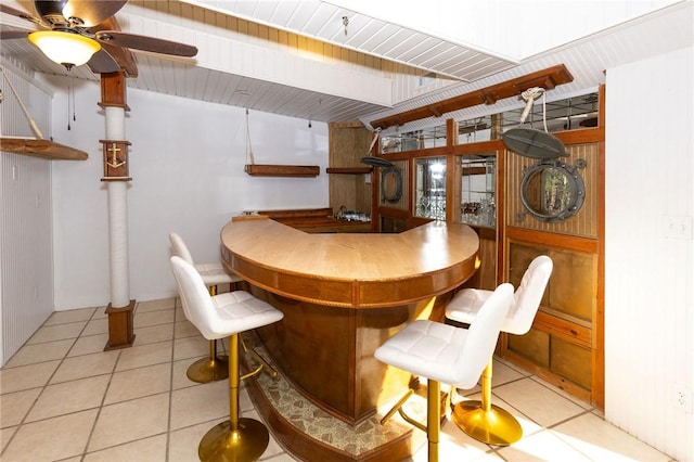 dining space featuring bar area, ceiling fan, and light tile patterned flooring