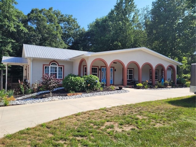 view of front facade featuring metal roof, a porch, concrete driveway, stucco siding, and a front yard