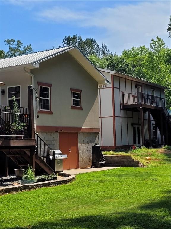 rear view of property with stairway, metal roof, a lawn, and stucco siding