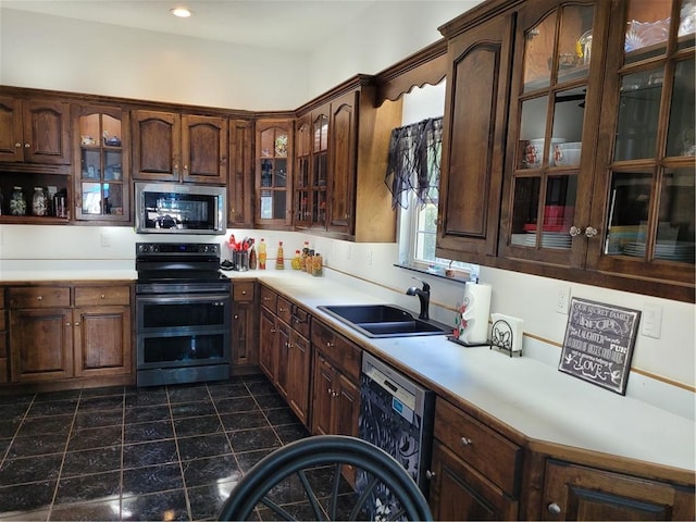 kitchen with appliances with stainless steel finishes, light countertops, a sink, and glass insert cabinets