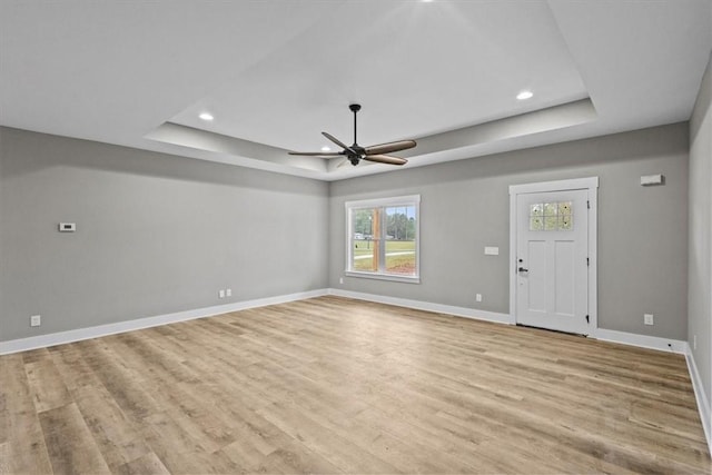 unfurnished living room with a healthy amount of sunlight, light hardwood / wood-style flooring, and a tray ceiling