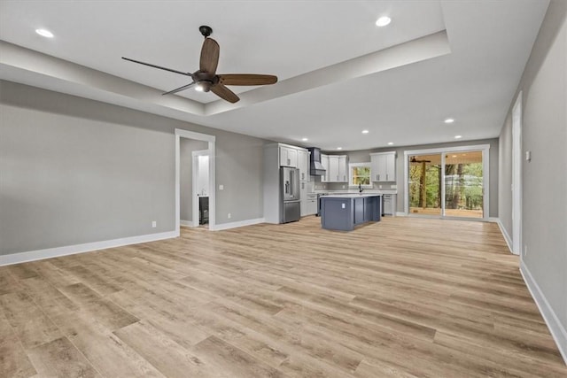 unfurnished living room with light wood-type flooring, a tray ceiling, and ceiling fan