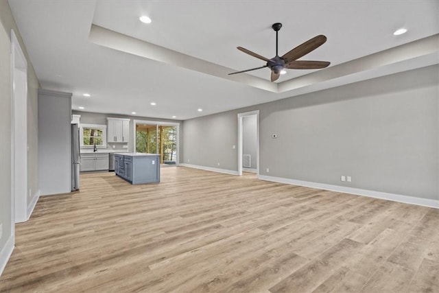 unfurnished living room with a raised ceiling, light hardwood / wood-style flooring, and ceiling fan