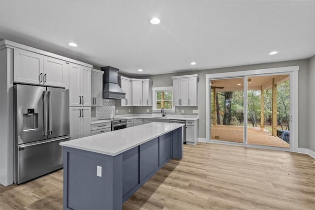 kitchen with appliances with stainless steel finishes, premium range hood, sink, light hardwood / wood-style flooring, and a kitchen island