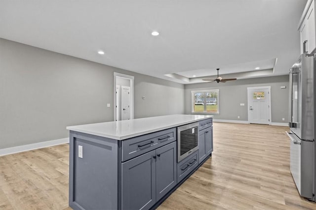 kitchen featuring appliances with stainless steel finishes, a tray ceiling, ceiling fan, light hardwood / wood-style flooring, and a center island