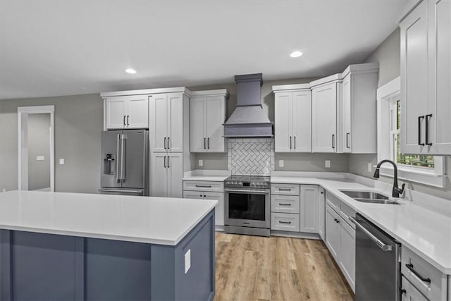 kitchen with premium range hood, sink, light hardwood / wood-style flooring, appliances with stainless steel finishes, and a kitchen island