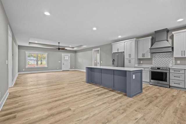 kitchen featuring appliances with stainless steel finishes, custom range hood, a tray ceiling, a center island, and gray cabinets