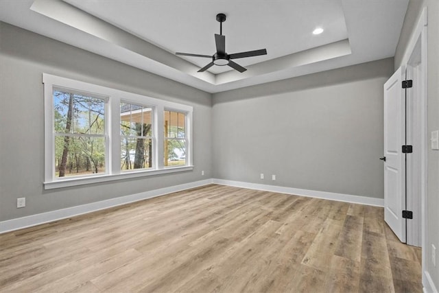 empty room with ceiling fan, a raised ceiling, and light wood-type flooring