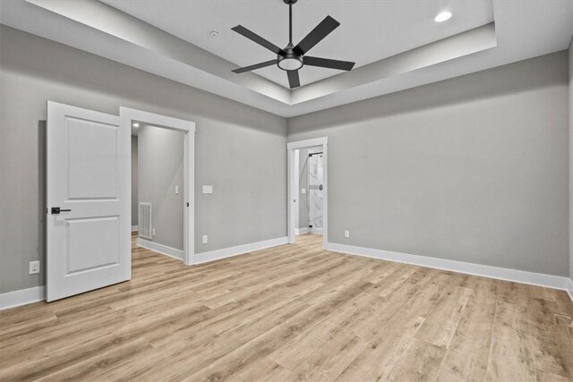 unfurnished room featuring ceiling fan, light hardwood / wood-style floors, and a tray ceiling