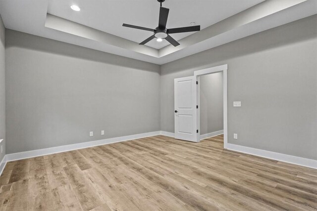 unfurnished room featuring ceiling fan, a raised ceiling, and light hardwood / wood-style flooring