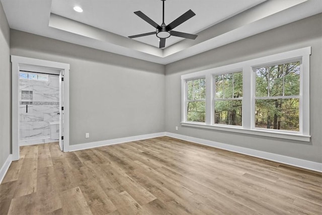 unfurnished room featuring light wood-type flooring, a tray ceiling, and ceiling fan