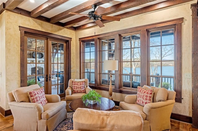 living area with ceiling fan, beamed ceiling, a water view, and wood-type flooring