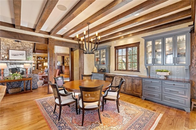 dining area with beamed ceiling, a notable chandelier, a fireplace, and light hardwood / wood-style flooring