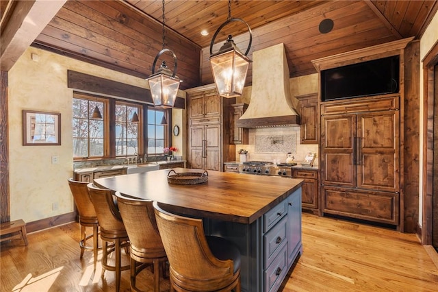 kitchen with wood ceiling, custom range hood, decorative light fixtures, butcher block countertops, and a kitchen island