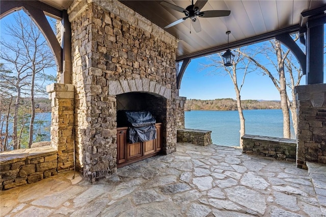 view of patio featuring an outdoor stone fireplace, ceiling fan, and a water view