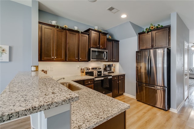 kitchen with sink, light hardwood / wood-style flooring, light stone countertops, appliances with stainless steel finishes, and kitchen peninsula