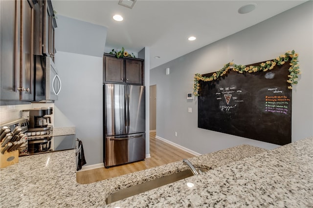 kitchen featuring dark brown cabinetry, light stone counters, light hardwood / wood-style flooring, and stainless steel appliances