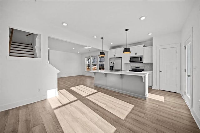 kitchen featuring appliances with stainless steel finishes, a breakfast bar, a large island with sink, decorative light fixtures, and white cabinets